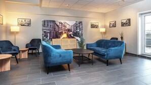 A modern lounge area with blue upholstered chairs, a wooden coffee table, and a large cityscape painting on the wall. - Thon Hotel Baronen (Ålesund)