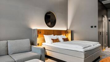 Habitación de hotel moderna con una cama grande, un sofá gris, una mesita y un cabecero de madera.