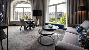 A modern hotel room with a large window, a round table, a sofa, and a flat-screen TV. - Karl Johan Hotel (Oslo)