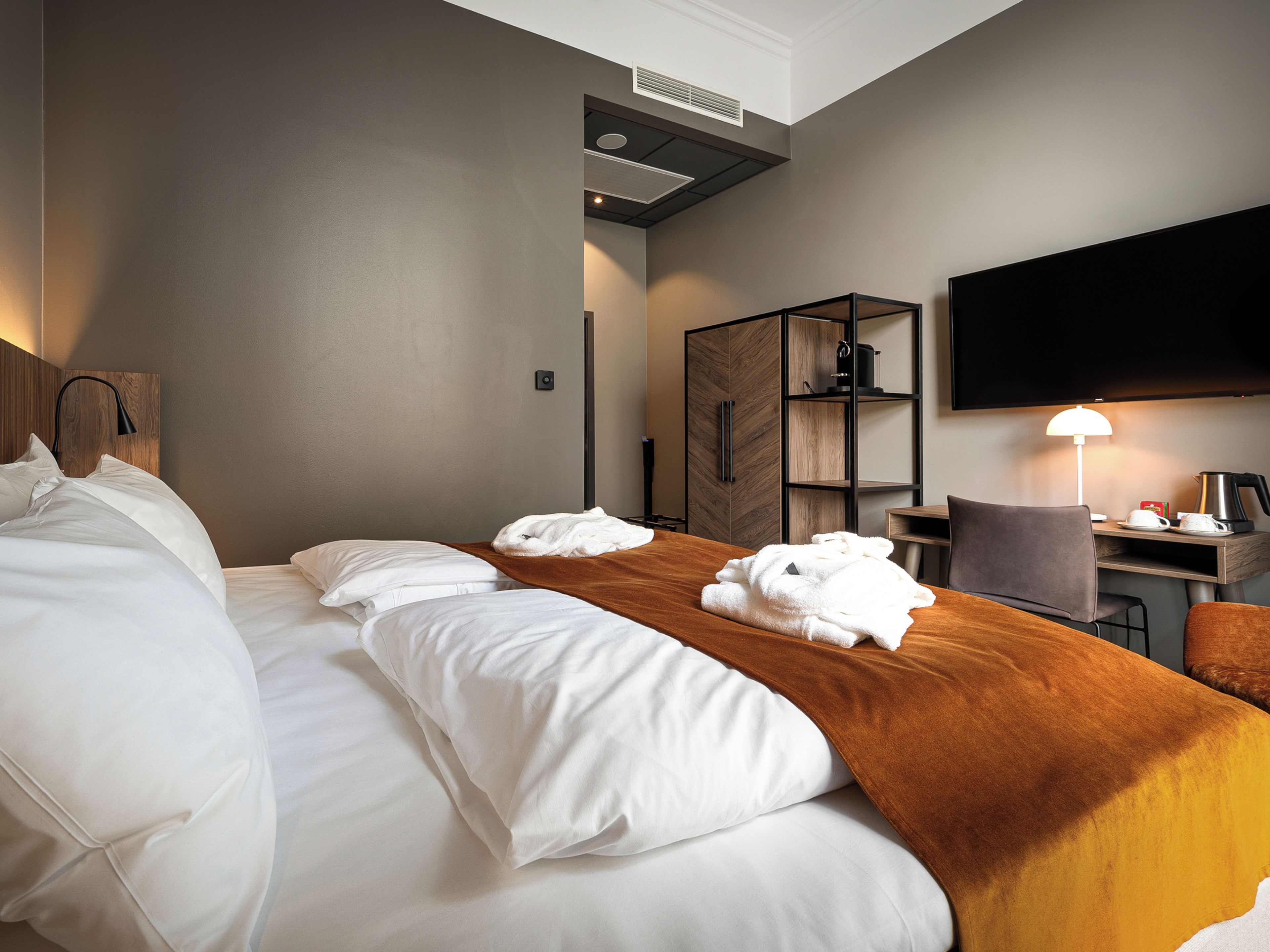 Habitación de hotel con una cama grande, cabecera de madera, televisor de pantalla plana montado en la pared, escritorio con una silla y cafetera.