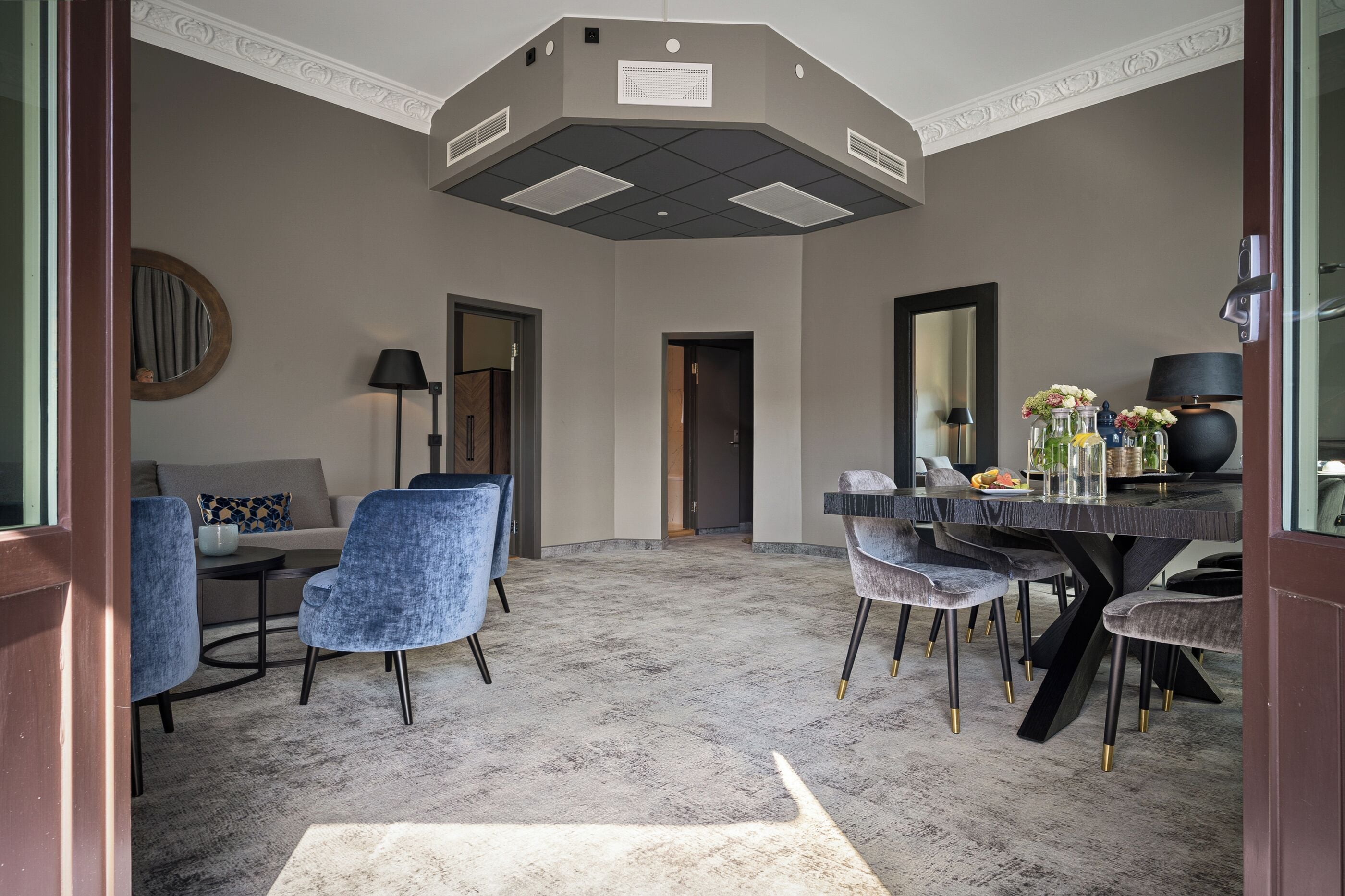 A modern dining area with a round table, blue upholstered chairs, and a dark floor lamp.