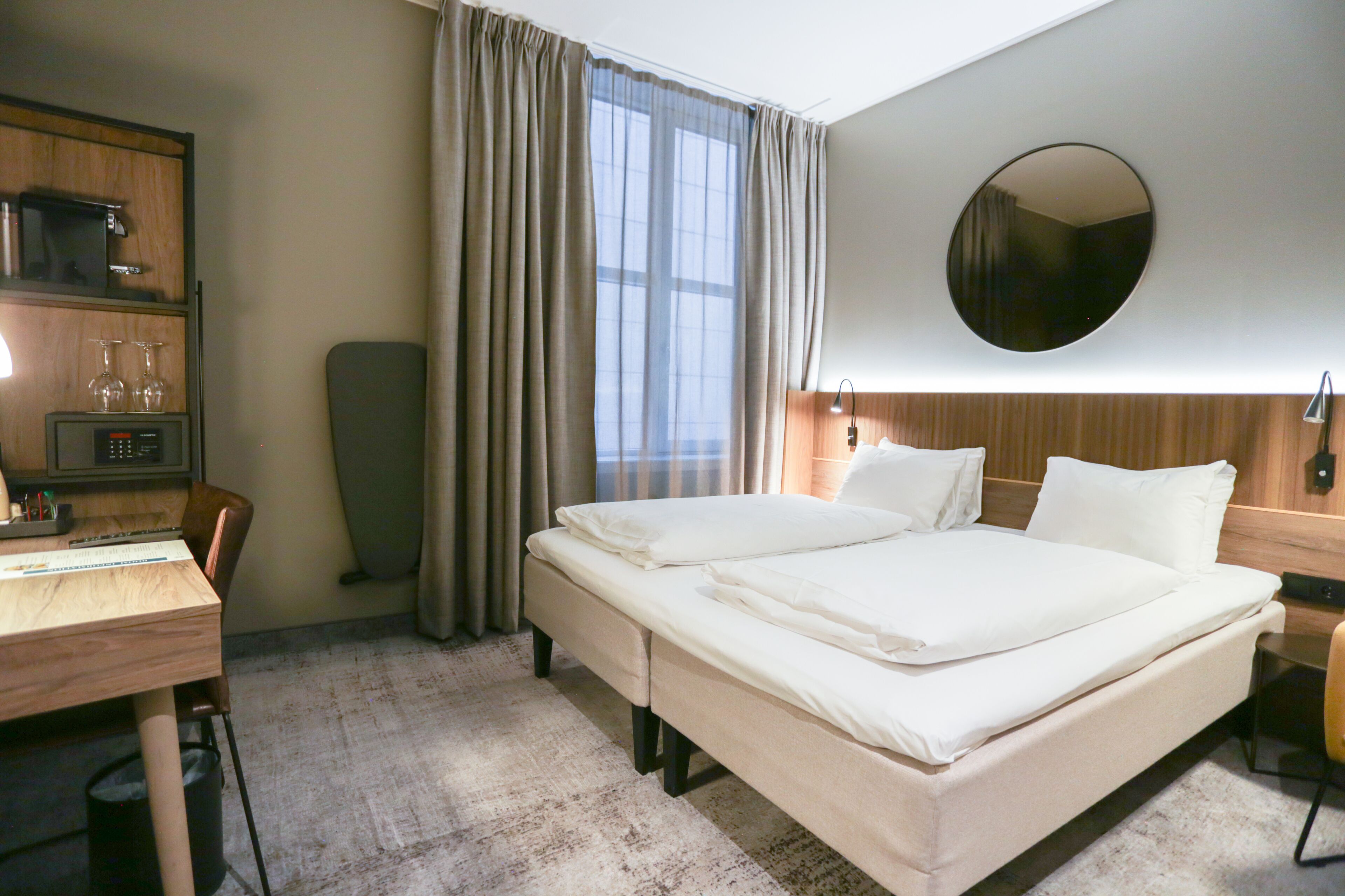 Una habitación de hotel con cama, escritorio, silla y un espejo en la pared.