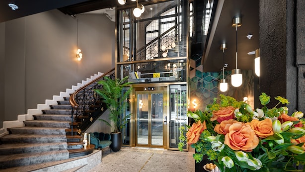 A modern hotel lobby with a marble staircase, a glass elevator, and a large floral arrangement. - Karl Johan Hotel (Oslo)