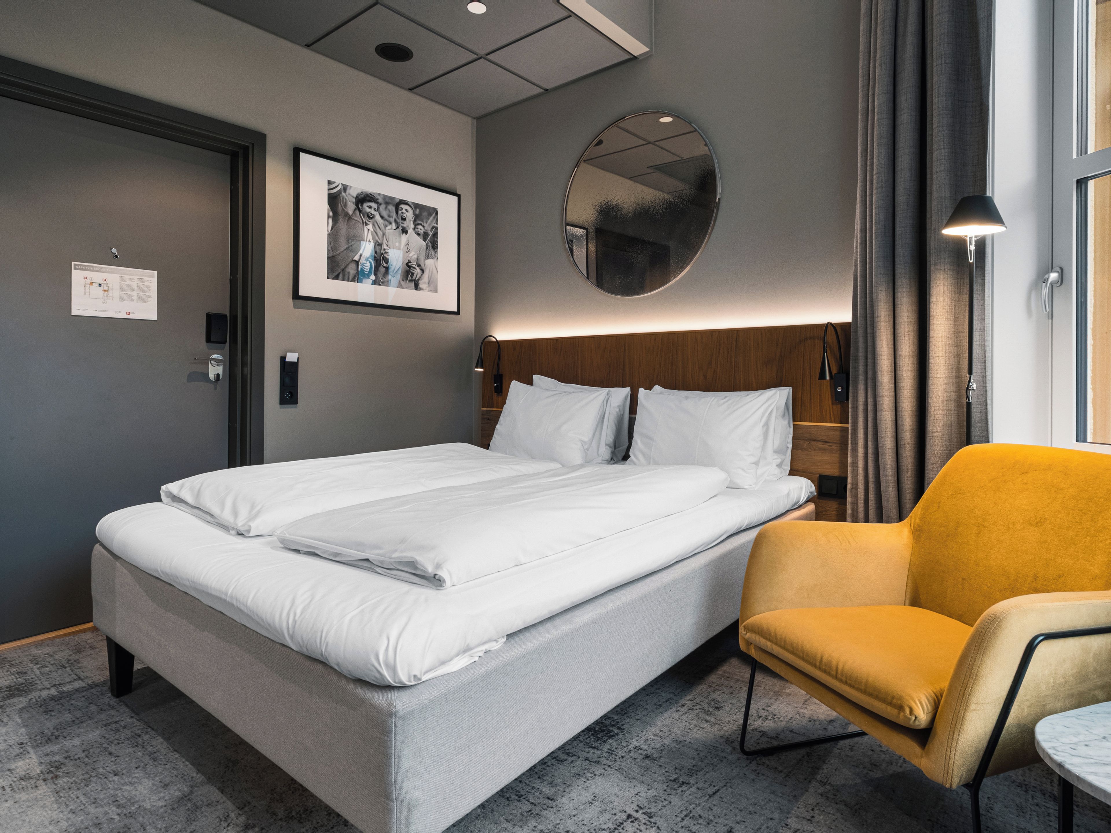 Een hotelkamer met een bed, een stoel, een spiegel en een schilderij aan de muur.