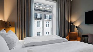 A hotel room with a bed, a chair, a desk, and a TV.