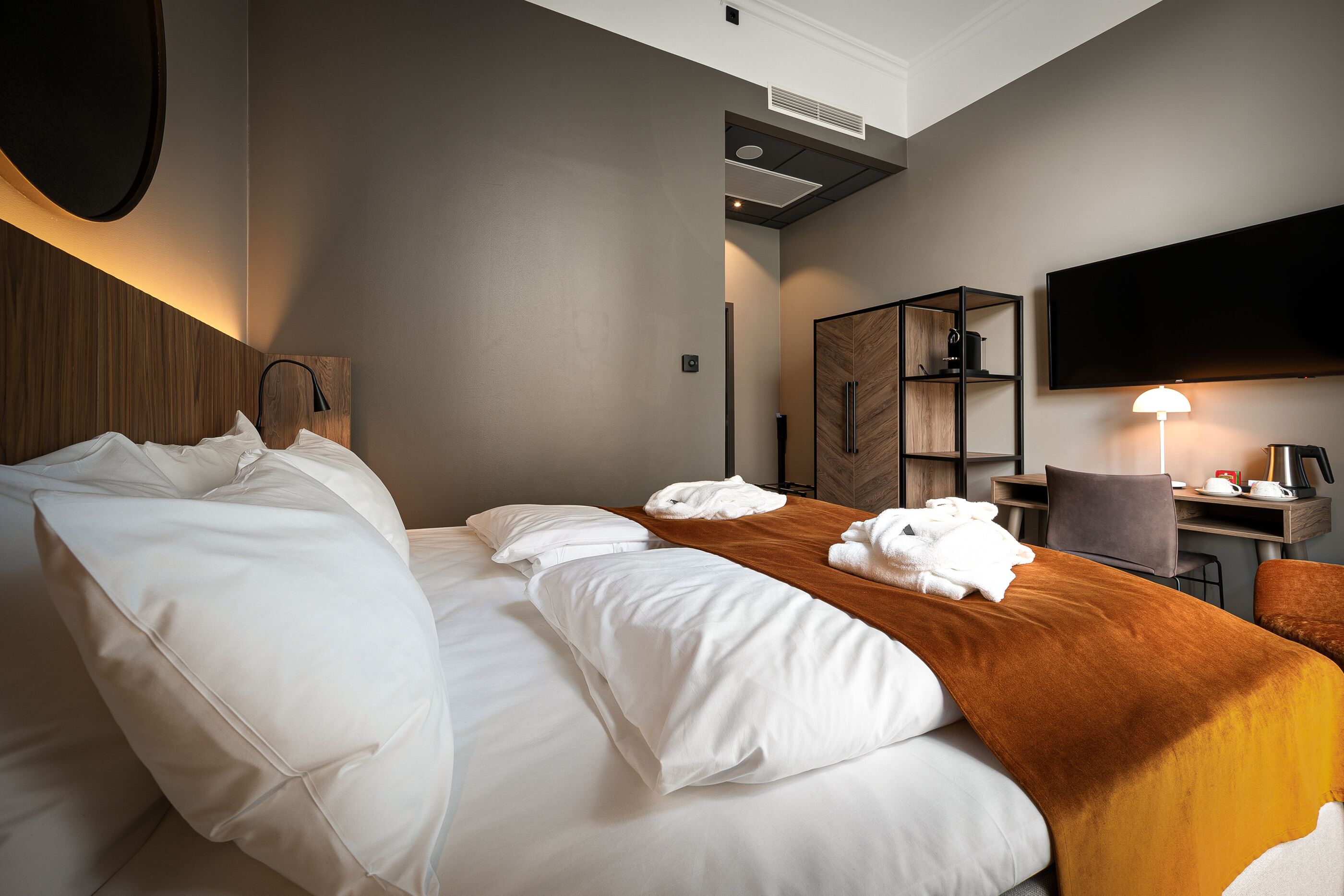 Quarto de hotel com cama grande, escrivaninha, cadeira, televisão e guarda-roupa.