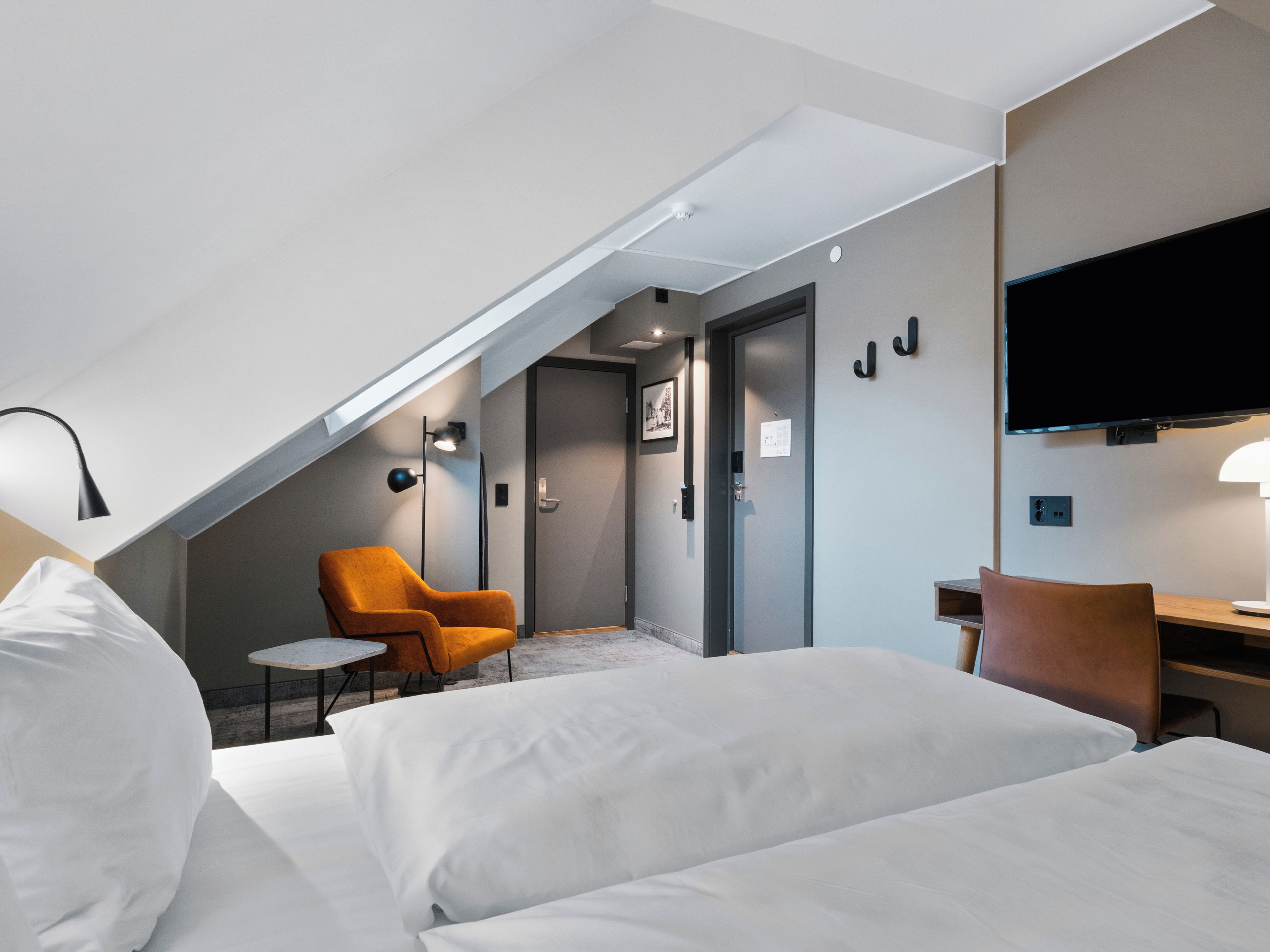 Una habitación de hotel con cama, dos sillas, escritorio, televisor y lámpara de techo.