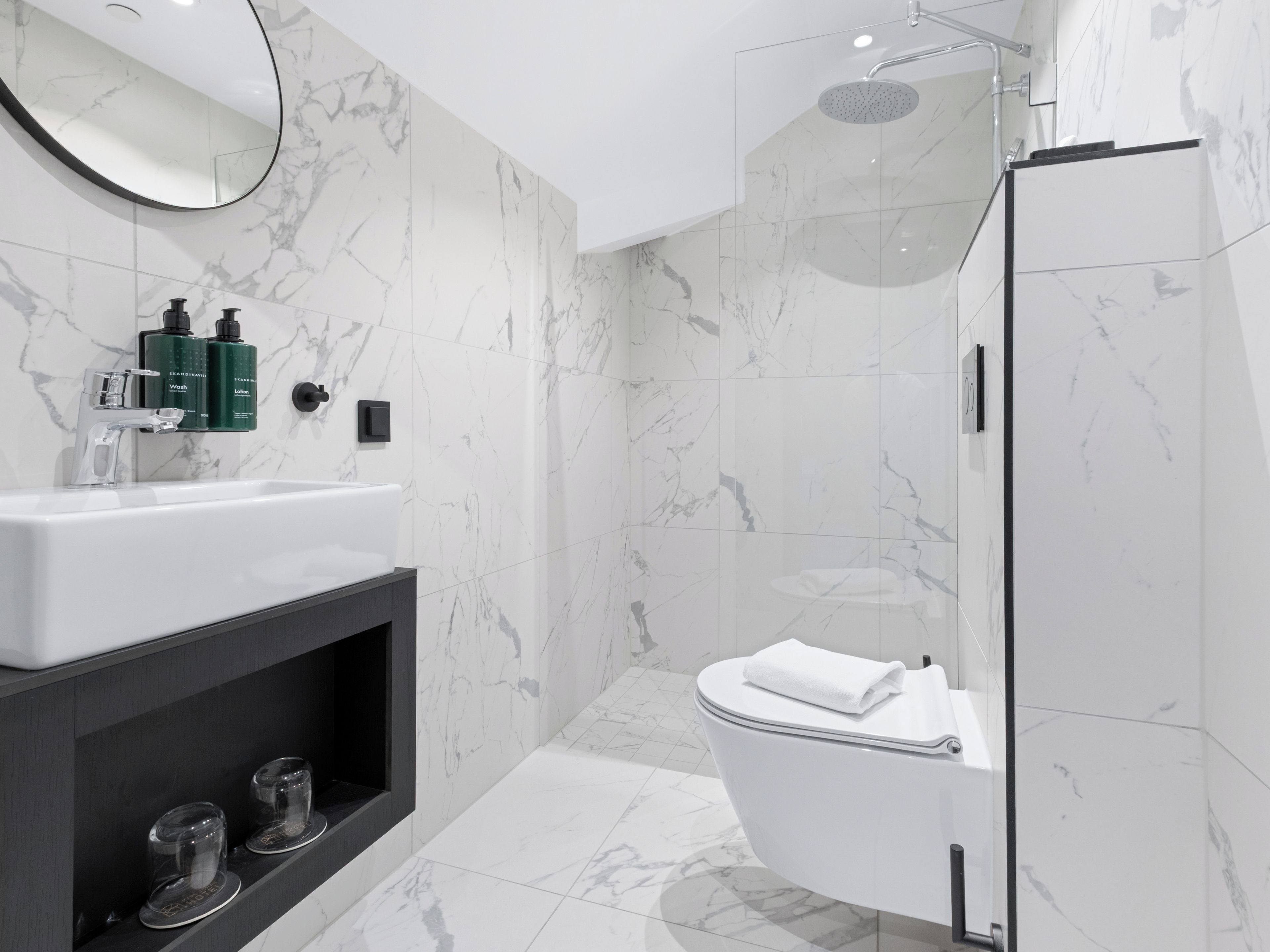 A modern bathroom with a marble sink, a toilet, and a shower enclosure.