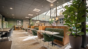A modern restaurant interior with green upholstered booths, round tables, and chairs. - Karl Johan Hotel (Oslo)