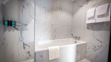 A modern bathroom with a marble shower wall, a white bathtub, and a towel rack with two towels.