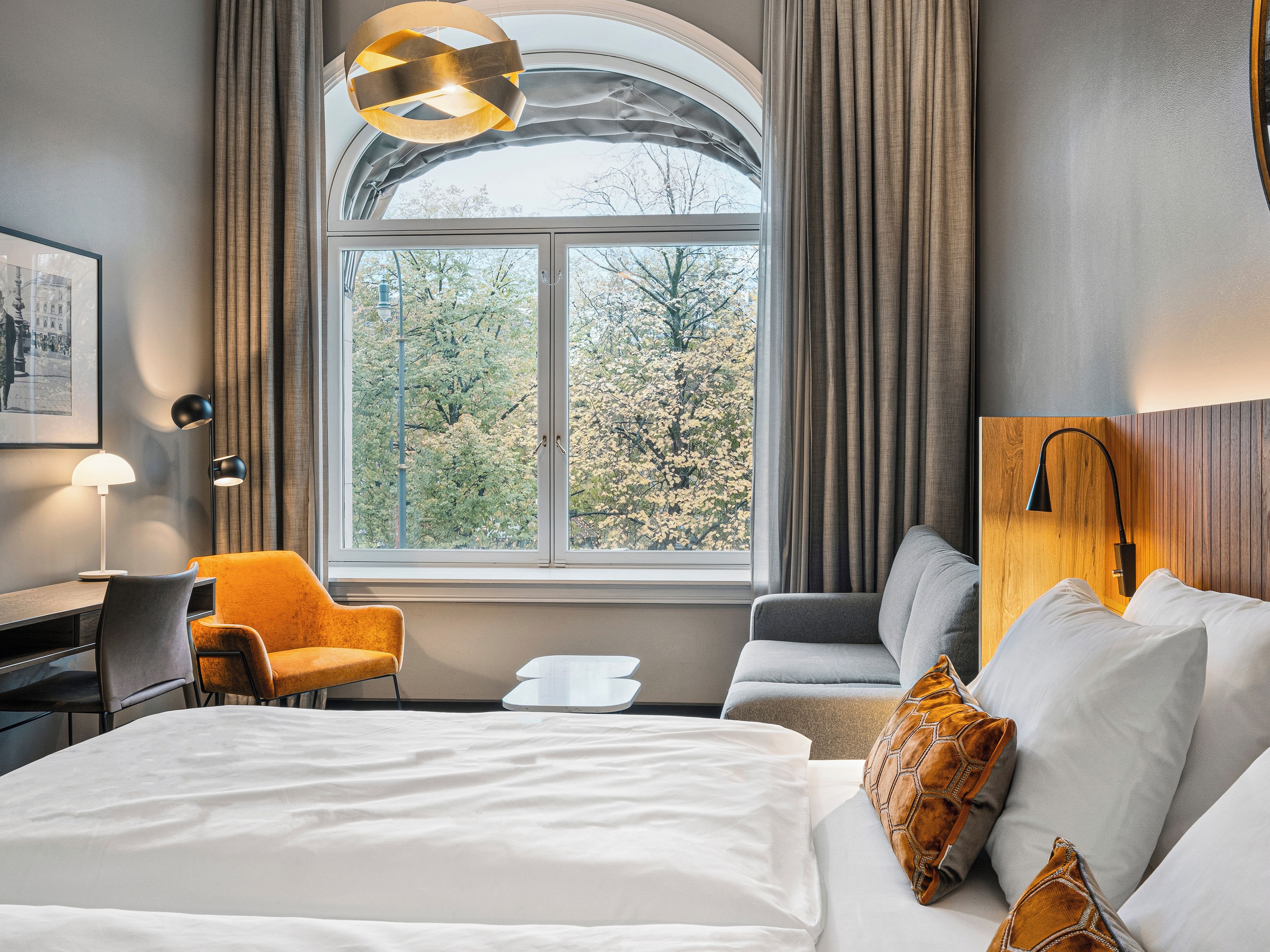 A hotel room with a large bed, a desk, a chair, and a view of trees through a window.