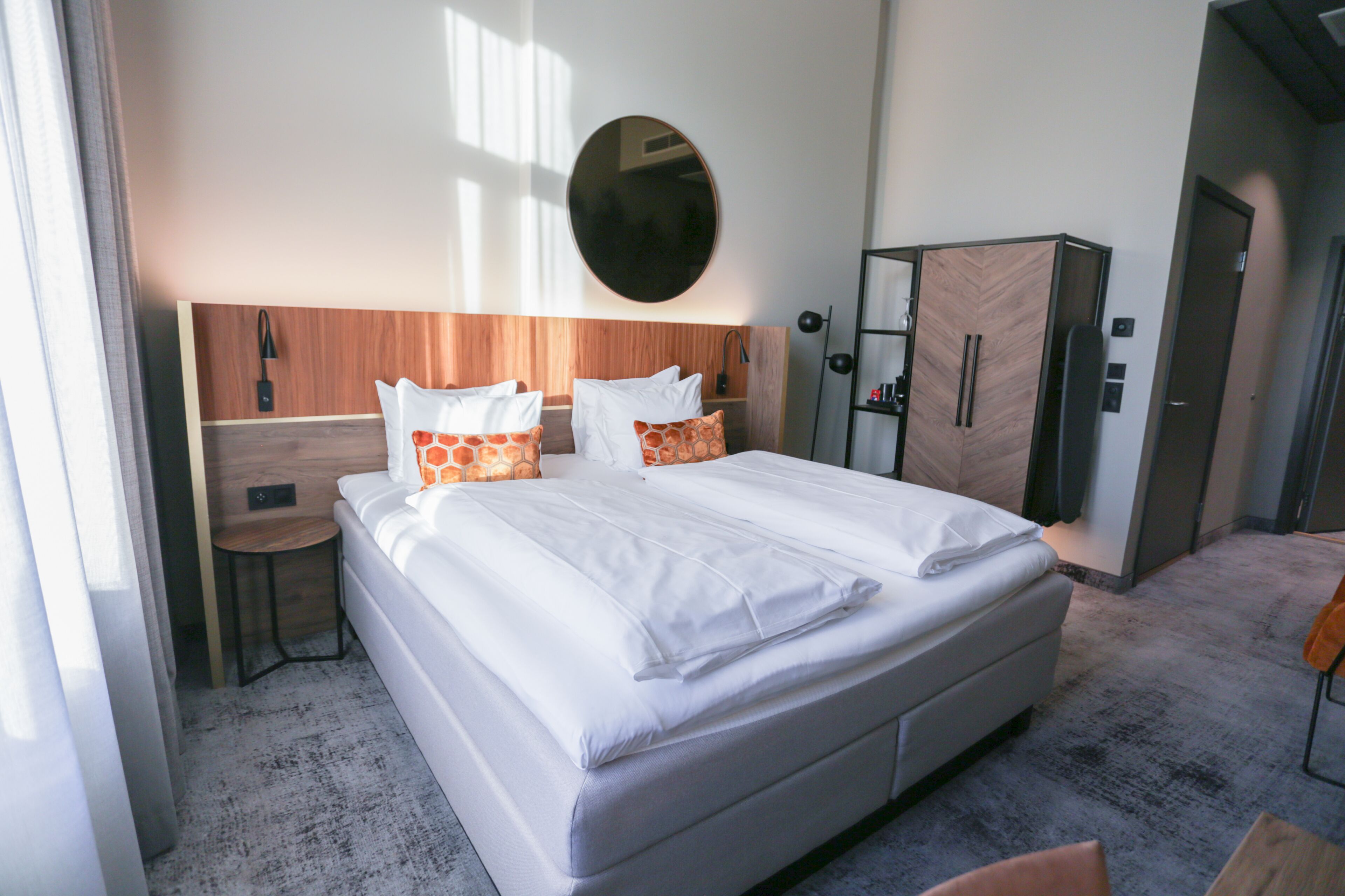 A hotel room with a large bed, a wooden headboard, a round mirror, a wardrobe, and a small table.