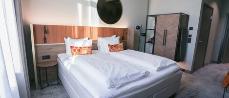 Una habitación de hotel con una cama grande, un cabecero de madera, un espejo redondo, un armario y una mesita.