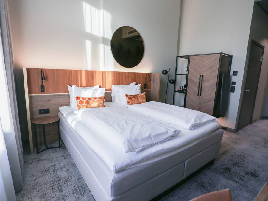 A hotel room with a large bed, a wooden headboard, a round mirror, a wardrobe, and a small table.