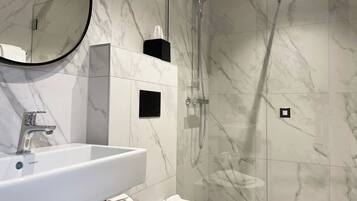 A modern bathroom with a marble floor, a white sink, a toilet, and a glass-enclosed shower.