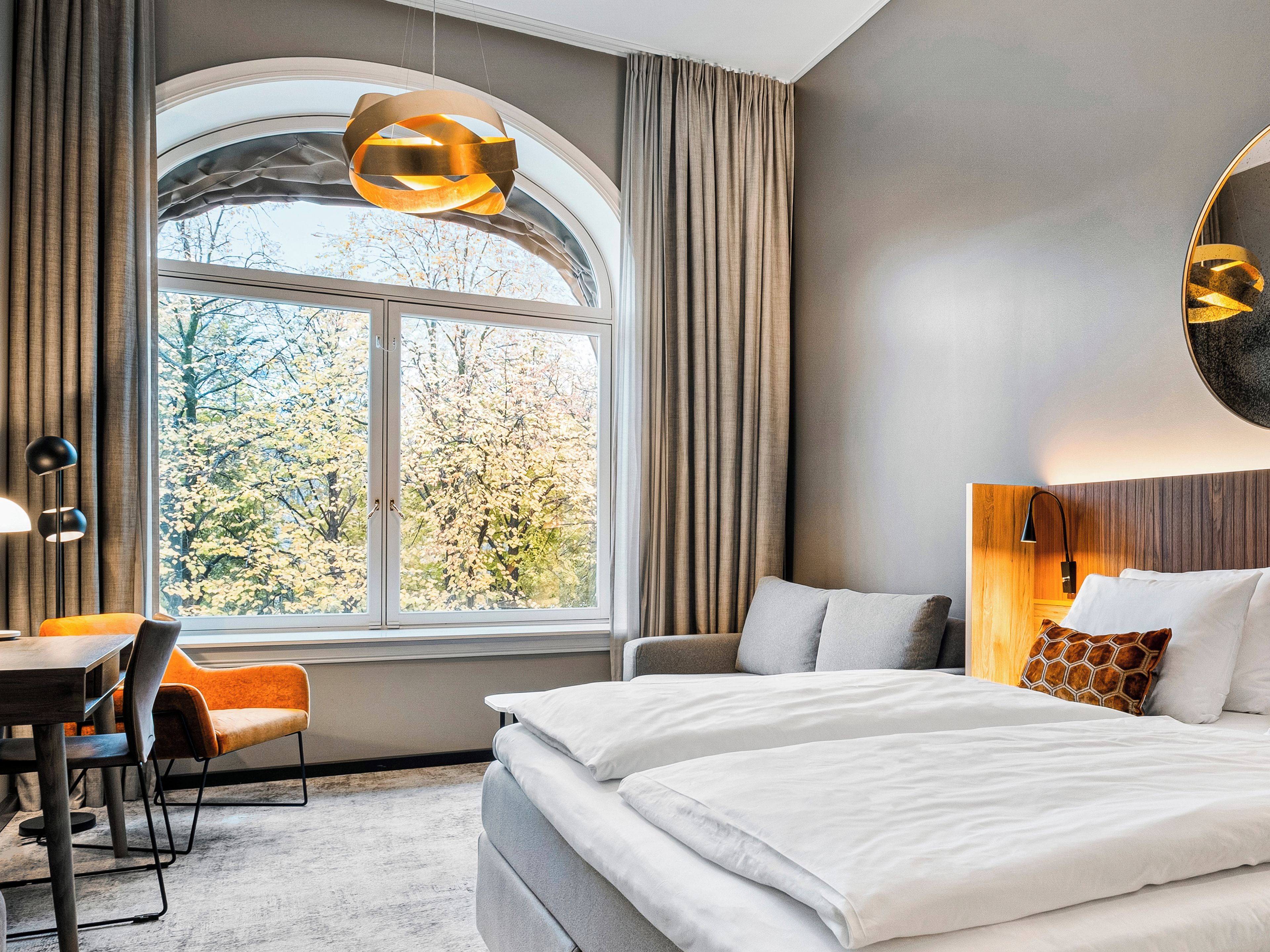 A hotel room with a large window, a bed, a desk, and a chair.
