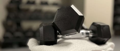Un par de mancuernas negras sobre una toalla blanca, con un fondo desenfocado de otras mancuernas.