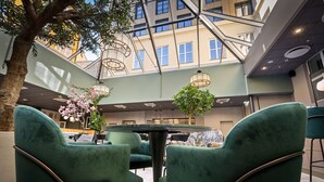 A modern indoor space with green upholstered chairs around a central table, a tree, and hanging light fixtures. - Karl Johan Hotel (Oslo)
