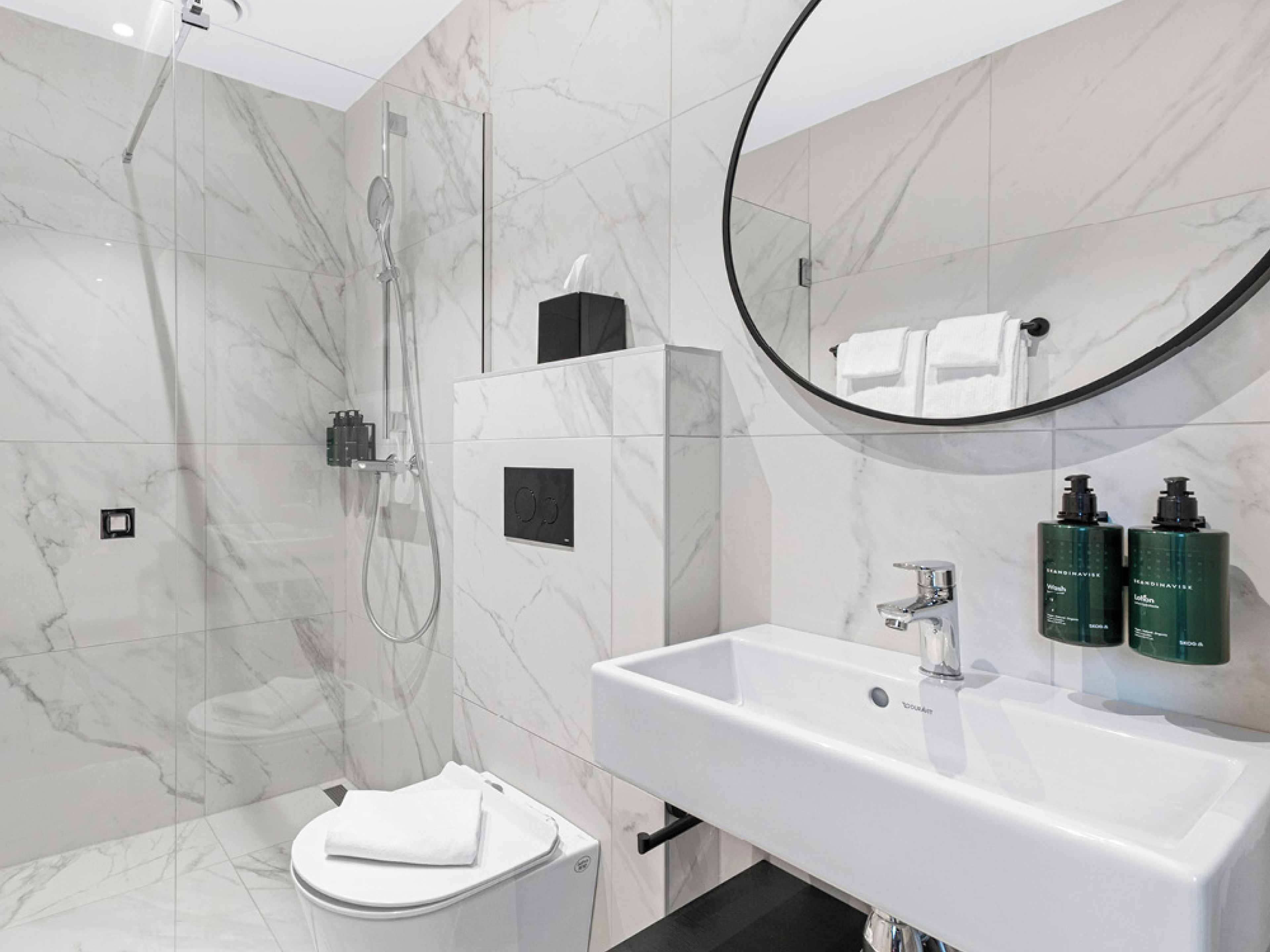 Un baño moderno con ducha, inodoro, lavabo y dispensadores de gel antibacterial.