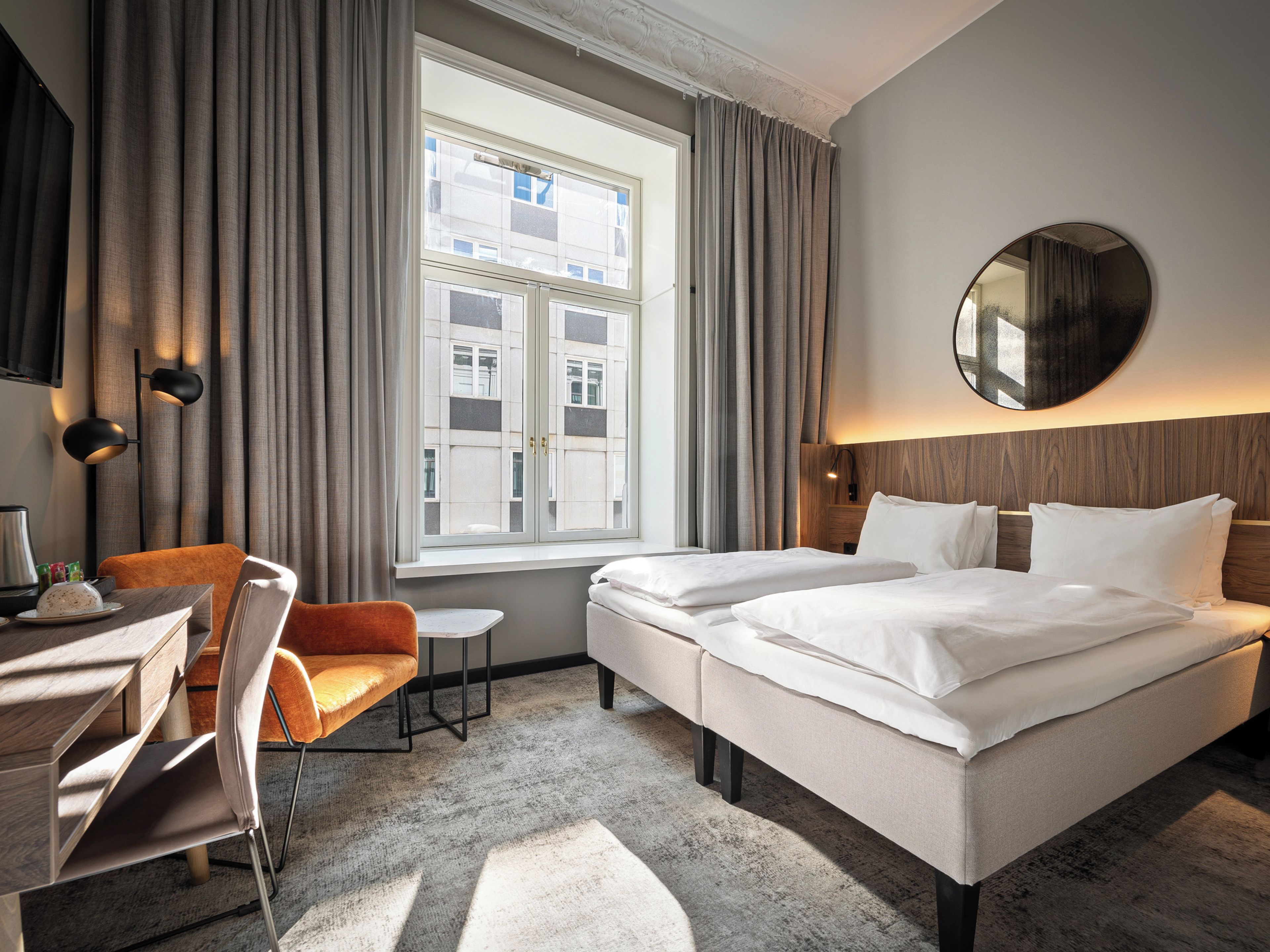Une chambre d’hôtel avec un lit, un bureau, une chaise, une petite table et une fenêtre avec des rideaux.