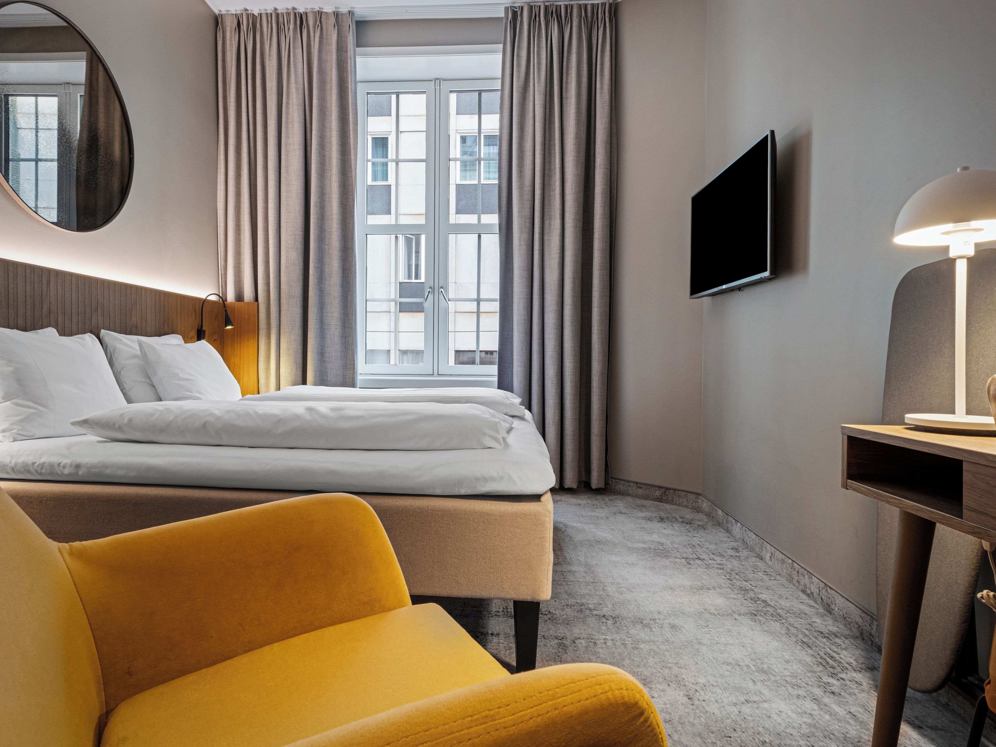 A hotel room with a bed, a desk, a chair, a television, and a window with curtains.