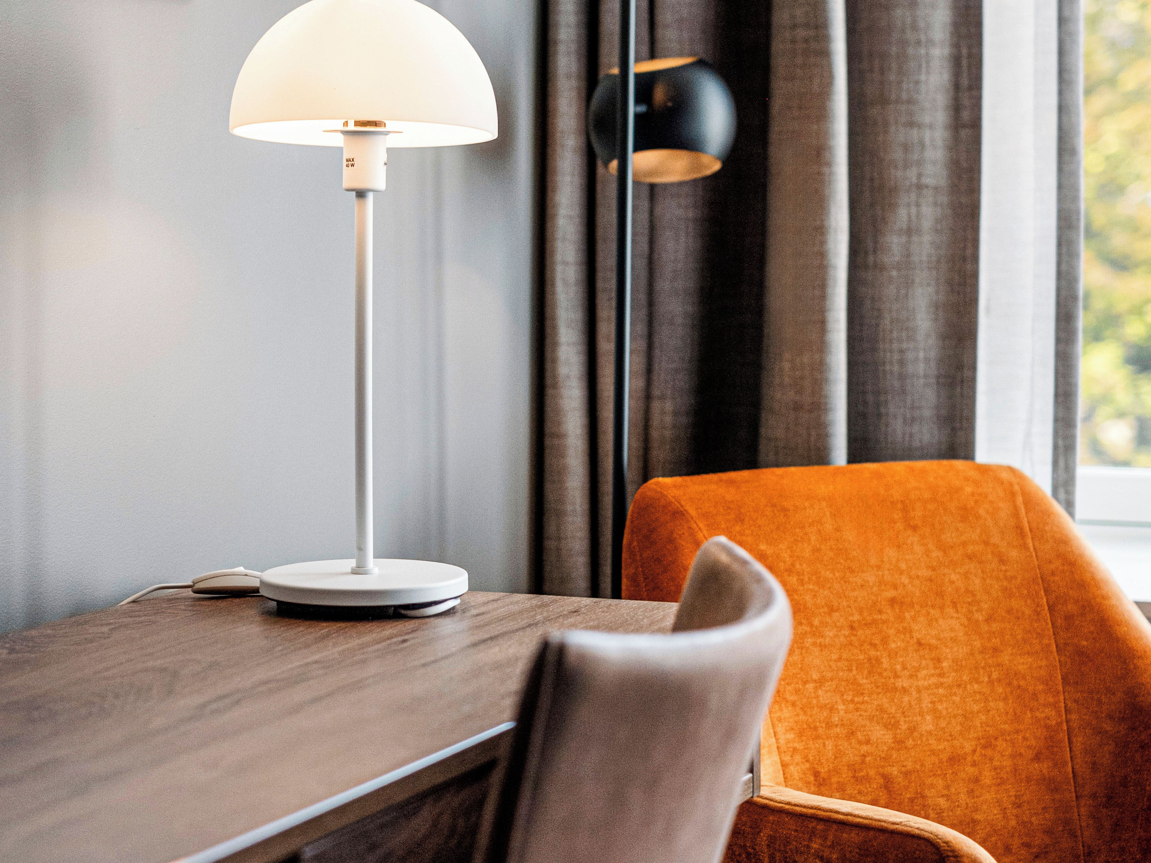 A modern room with a wooden desk, a white lamp, and an orange chair.