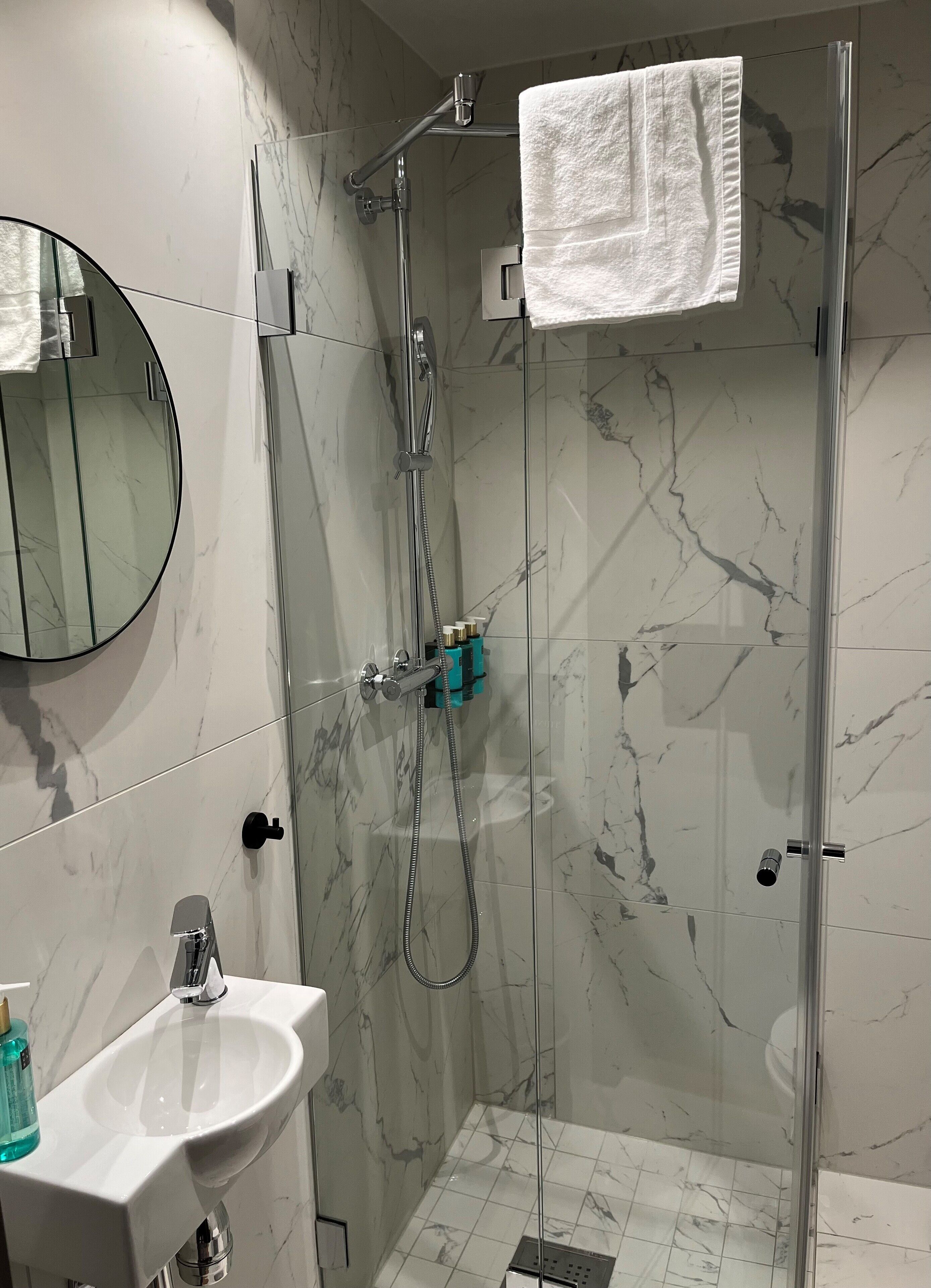A modern bathroom with a glass-enclosed shower, a round mirror, and a white sink.
