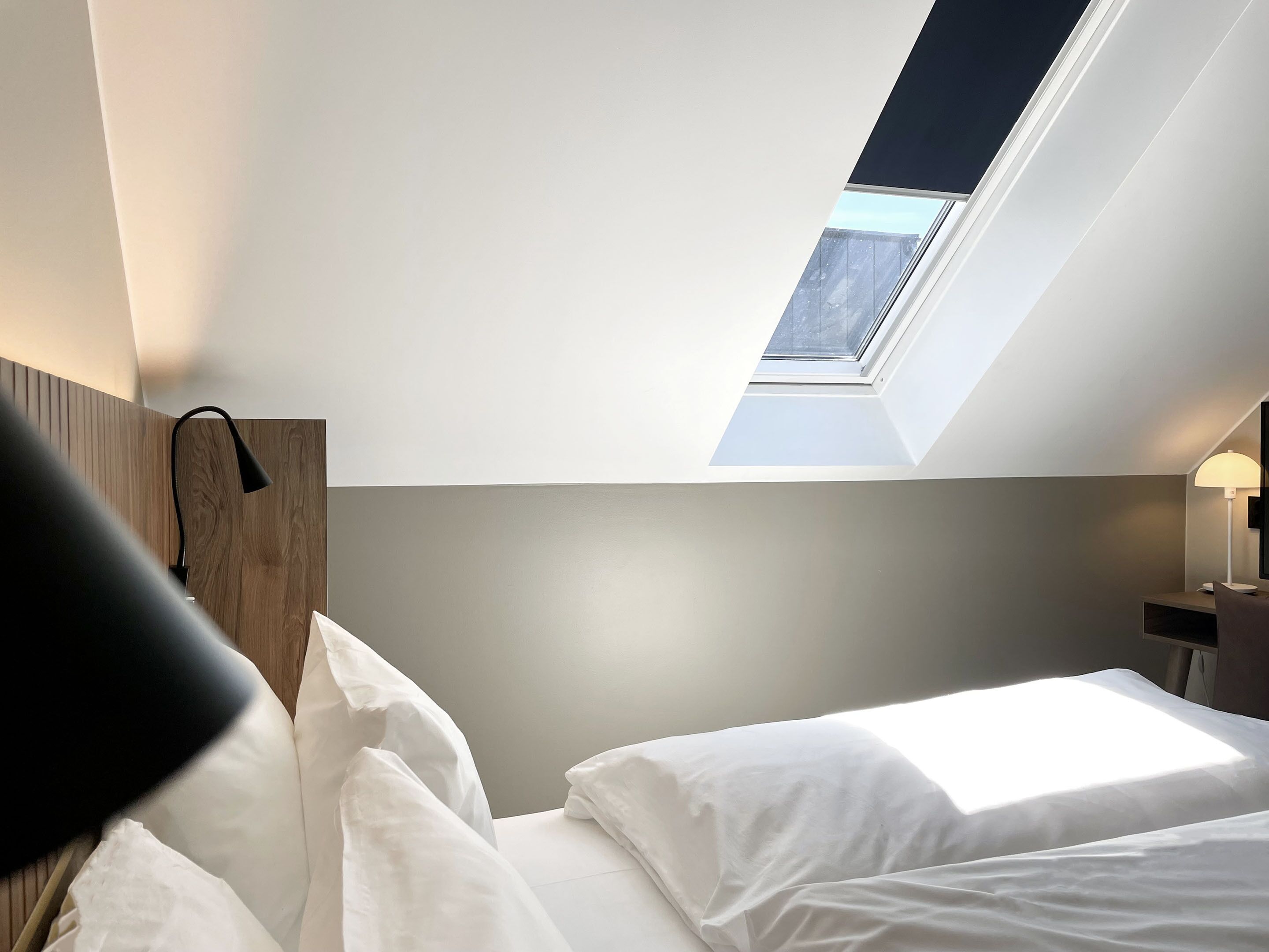 A bedroom with a skylight, a bedside lamp, and a nightstand.