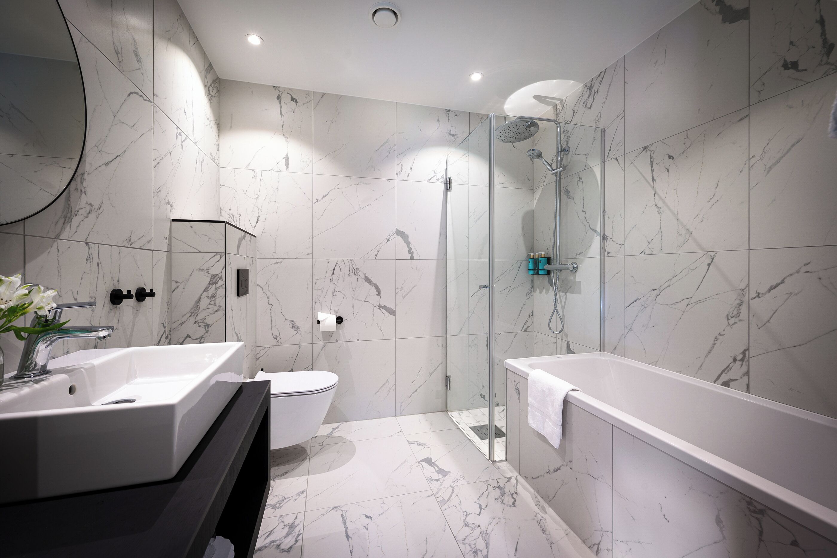 A modern bathroom with a marble floor, a large bathtub, a glass-enclosed shower, and a toilet.