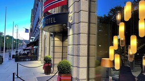 A hotel entrance with a sign, a glass door, and outdoor seating with tables and chairs. - Karl Johan Hotel (Oslo)
