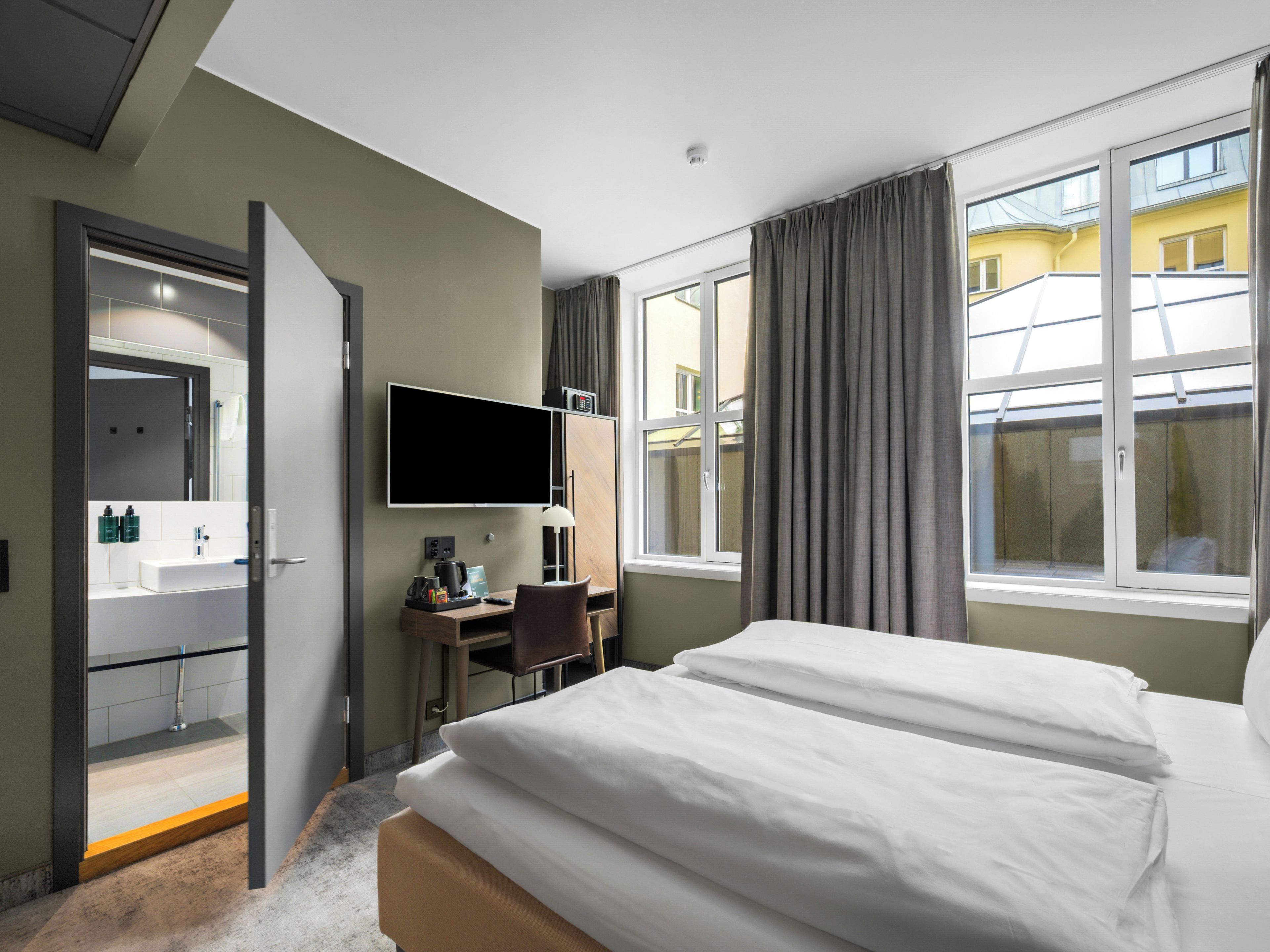 Une chambre d’hôtel équipée d’un lit, d’un bureau, d’une chaise, d’une télévision et d’une salle de bain avec un miroir et un lavabo.
