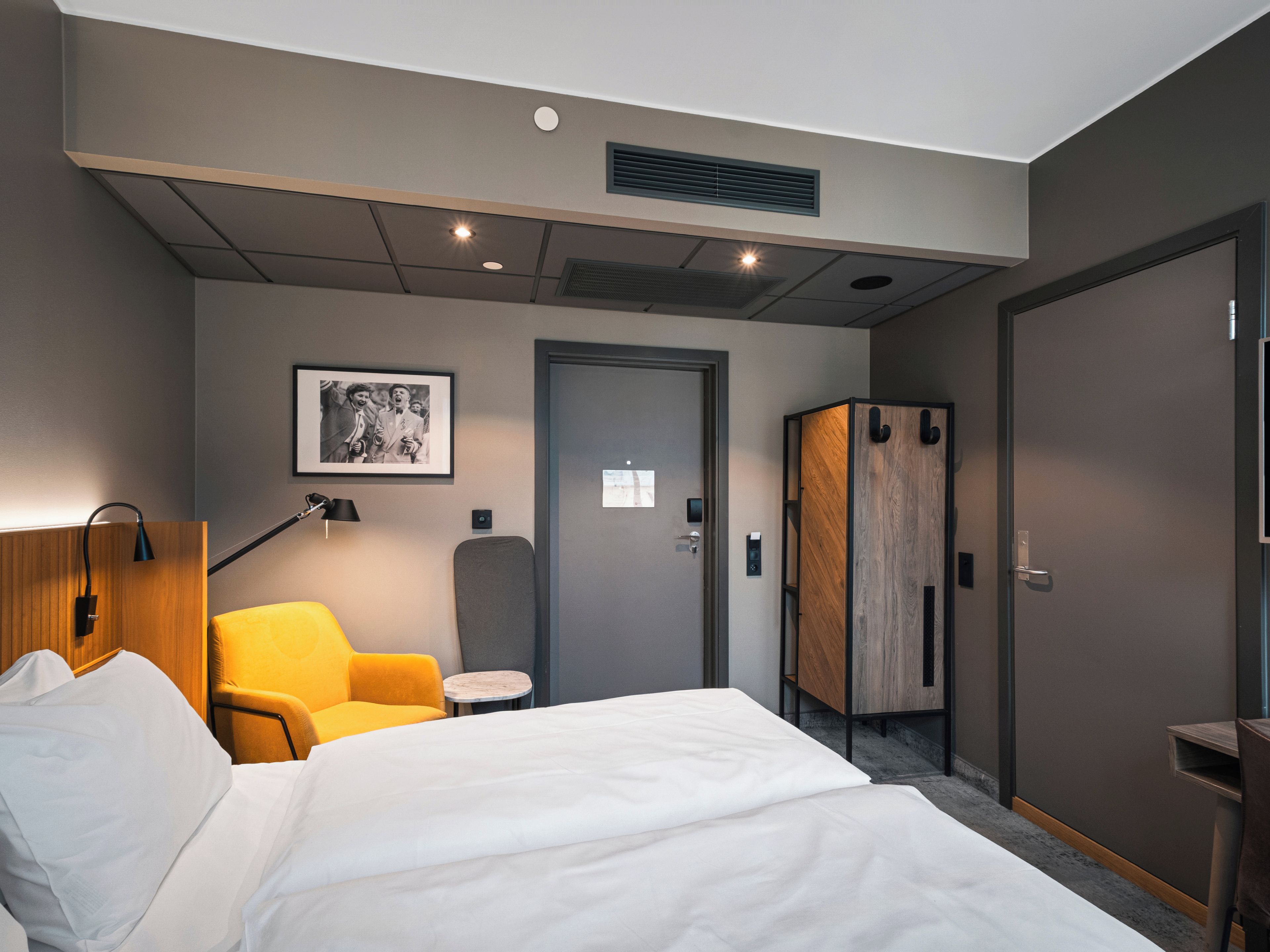 A hotel room with a bed, a desk, a chair, a wardrobe, and a picture on the wall.