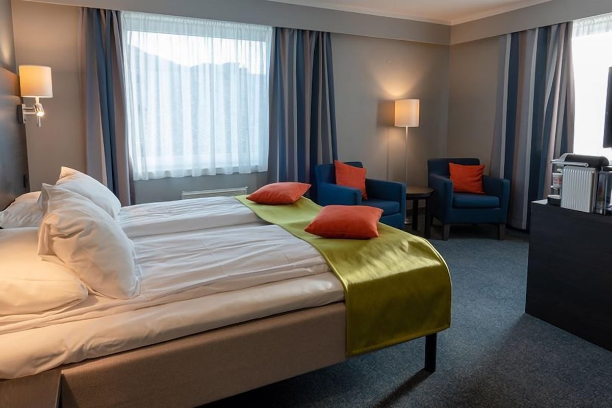 Una habitación de hotel con una cama grande, dos sillones, un escritorio y un radiador.
