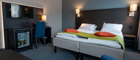 A hotel room with a bed, a TV, a desk, and a minibar.