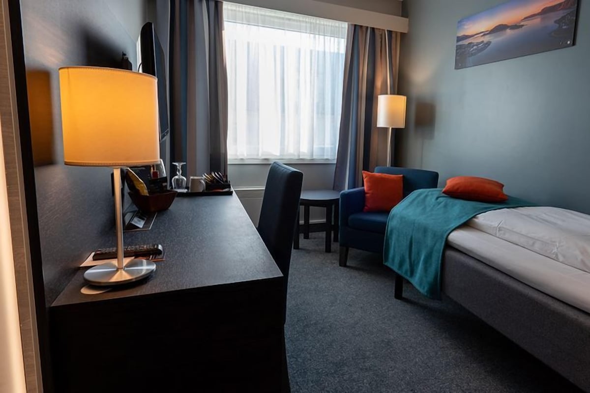 Habitación de hotel con escritorio, silla, cama y un cuadro en la pared.