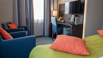 Une chambre d’hôtel comprenant un lit, deux fauteuils, un bureau, une télévision, un mini-réfrigérateur et une machine à café.