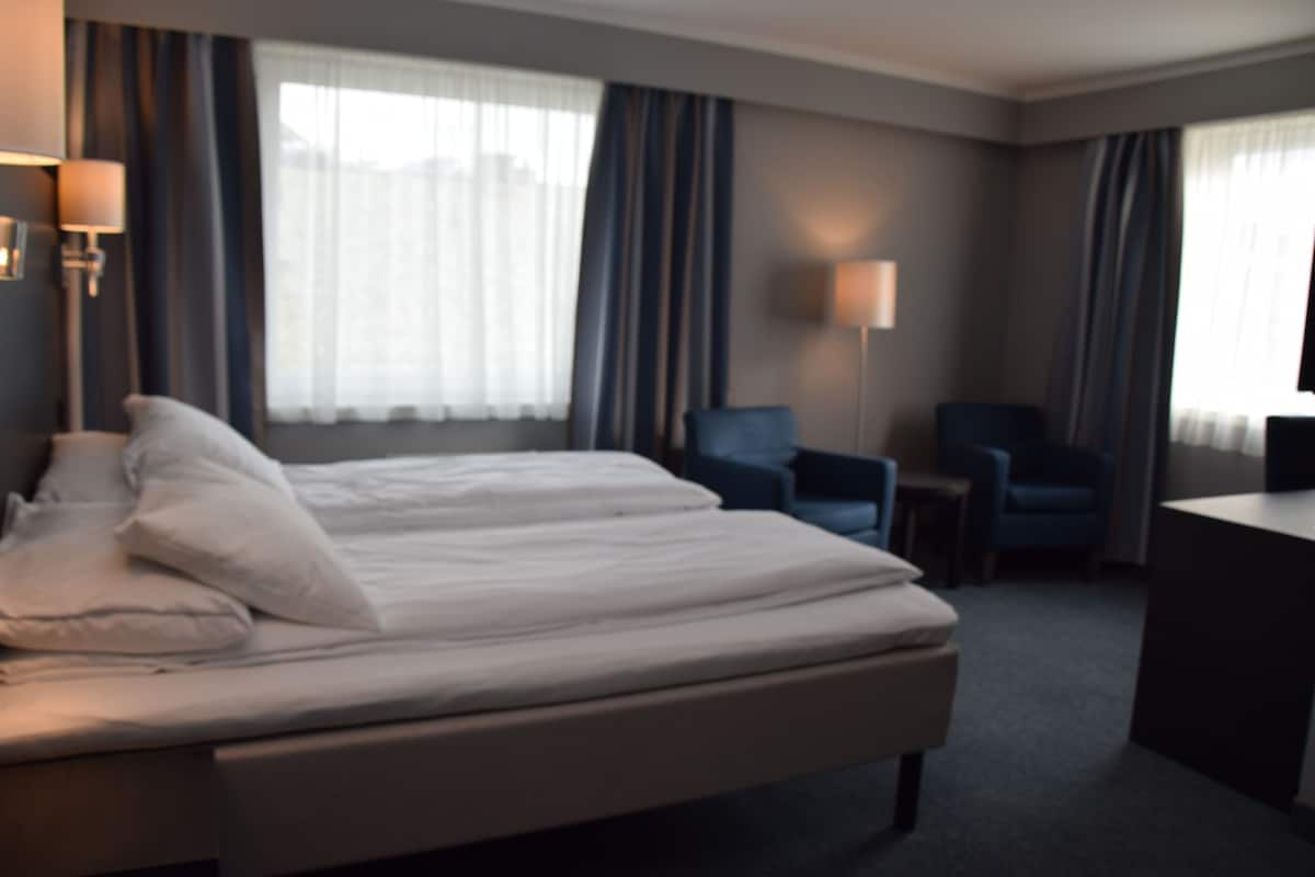 A hotel room with a bed, two chairs, a desk, and a TV.