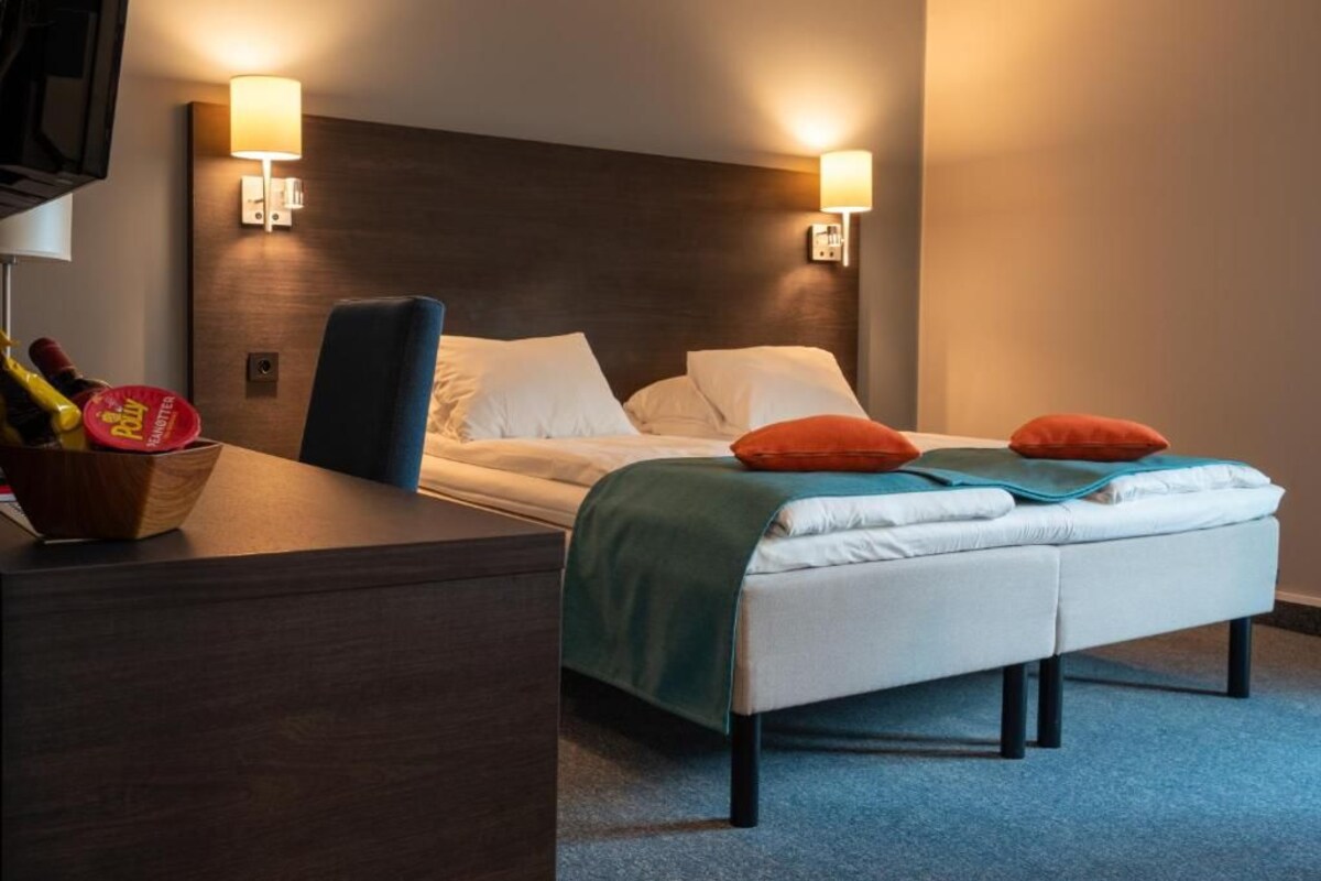 Una habitación de hotel con cama, mesitas de noche y lámparas de pared.