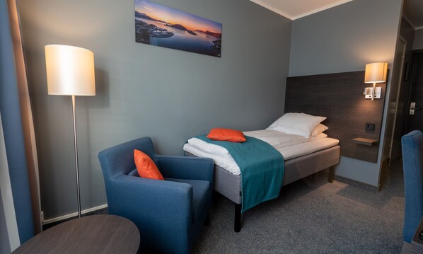 Ein Hotelzimmer mit Bett, Sessel, Schreibtisch und einem Bild an der Wand.
