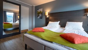 A modern hotel room with a large bed, a mirror, and a view of the mountains. - Thon Hotel Måløy (Kinn)