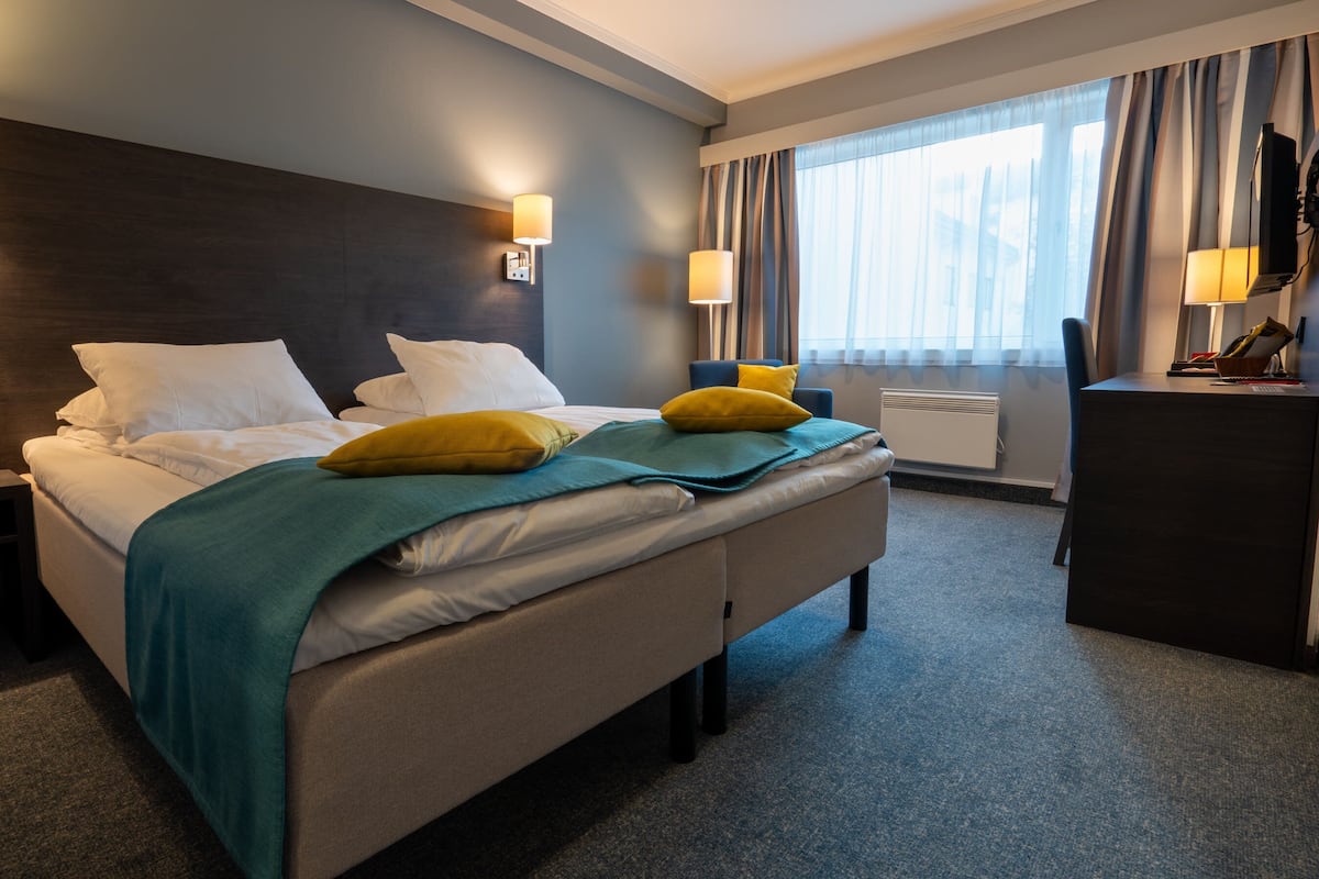 A hotel room with a bed, bedside lamps, a desk, and a window with curtains.