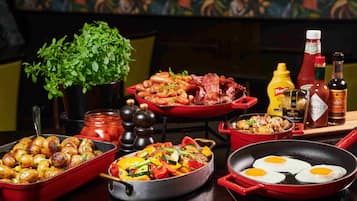 A variety of dishes including roasted potatoes, sautéed vegetables, and eggs in a pan, with condiments and a potted plant in the background.
