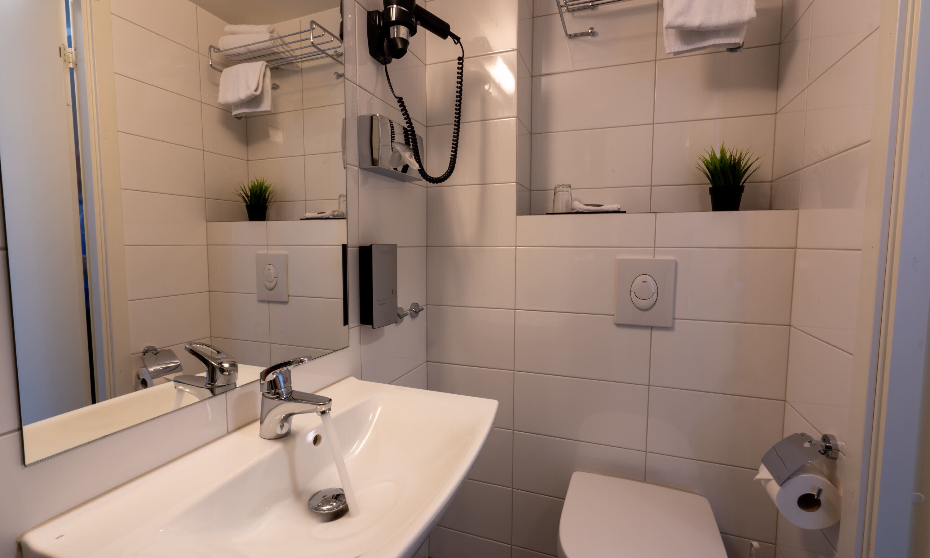 A modern bathroom with a sink, mirror, towel rack, and toilet.