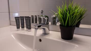 A bathroom sink with running water, a potted plant, and toiletries in the background.