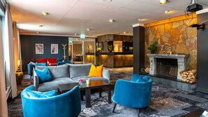 En modern entréhall med en eldstad i sten, blå och grå sittmöbler och ett köksområde i bakgrunden.