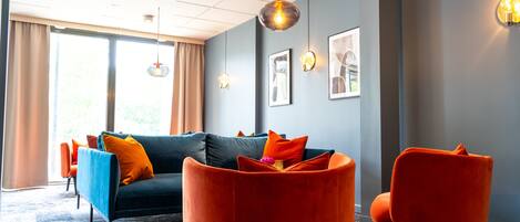 A modern living room with a dark blue sofa, orange armchairs, and a patterned carpet.
