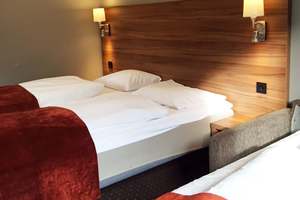 A hotel room with a large bed, two bedside tables, and a headboard with wall-mounted lamps.
