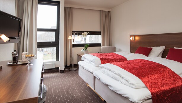 Ett hotellrum med två sängar, en TV, ett skrivbord med en kaffebryggare och ett fönster med gardiner.