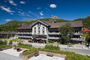 Un gran hotel con múltiples balcones y una entrada central, rodeado de vegetación exuberante y montañas al fondo.