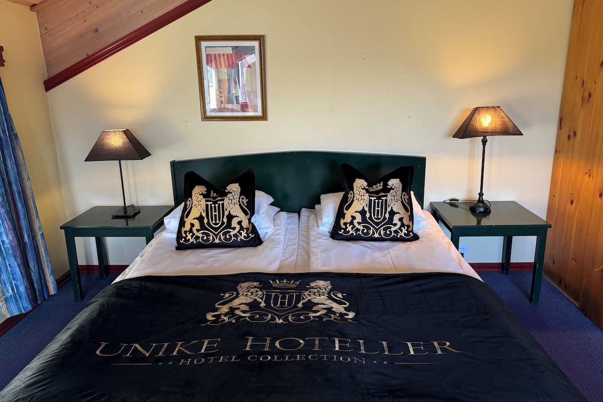A hotel room with a bed, two nightstands, two lamps, a framed picture on the wall, and a bedspread with the hotel name.